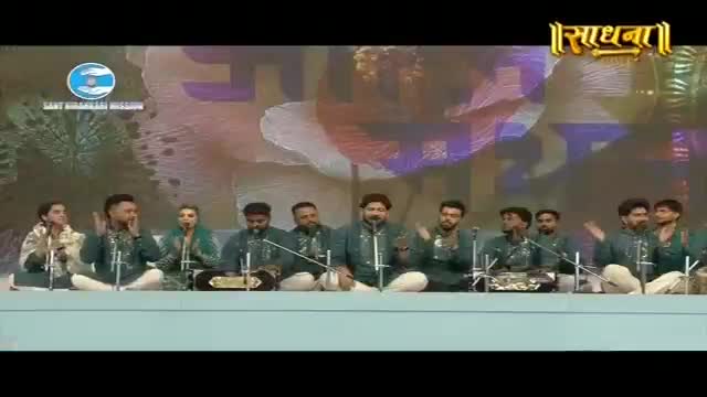 A group of musicians sits on a stage, their instruments laid out before them. The lead singer, in the center, gestures with his hands as he sings into the microphone.