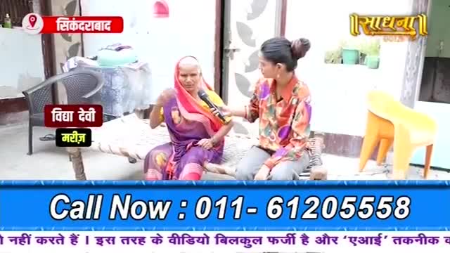 A woman in a colorful sari is being interviewed by a reporter holding a microphone. The reporter gestures with her free hand as she speaks.
