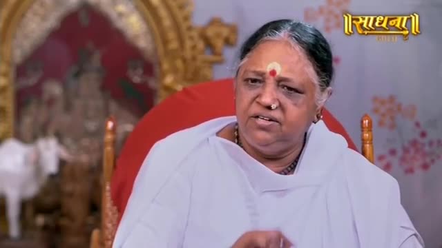 A woman with a red bindi on her forehead speaks animatedly, her white garment framing her face. Behind her, a blurred image of a deity and a white bull stands within an ornate setting.