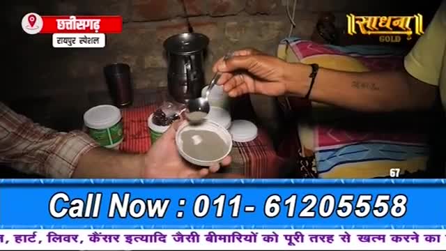 A hand scoops a grey powder from a small container into another, wider one. The scene is lit by a dim bulb, and a logo for "Sadhna Gold" is visible in the background.