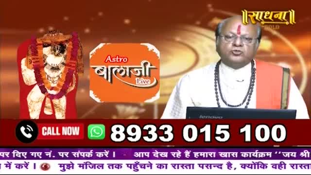A man in traditional Indian attire speaks, a large devotional image behind him. A phone number flashes across the bottom of the screen, inviting calls.
