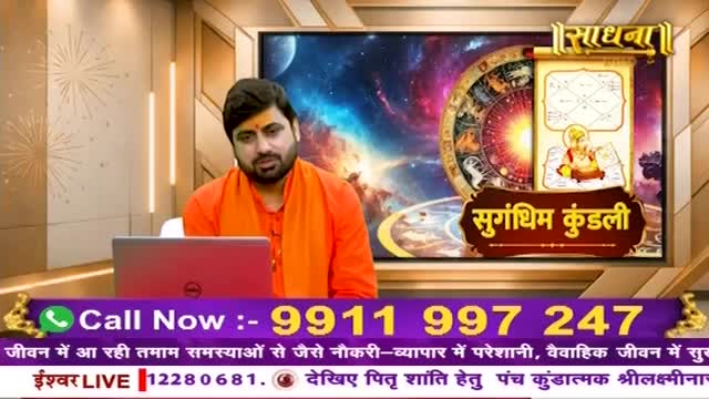 A man in an orange robe sits before a laptop, a cosmic backdrop behind him. A large screen displays astrological charts and the Sadhna logo.