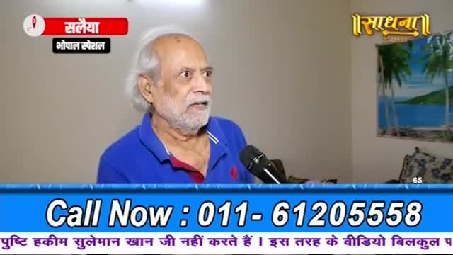 An older man with white hair and a beard speaks into a microphone. A banner at the bottom of the screen displays a phone number.