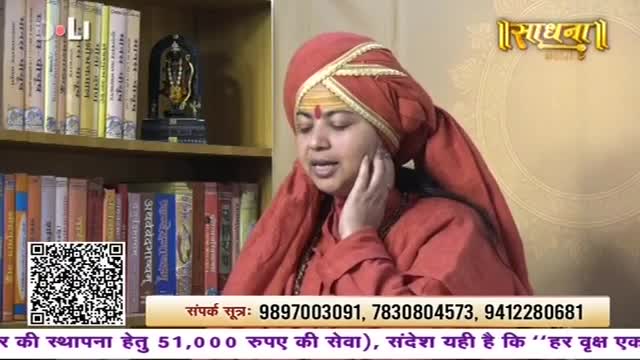 A woman in a red turban and robe speaks, her hand touching her cheek. Behind her, shelves are packed with books, and a small statue of a deity sits on the top shelf.
