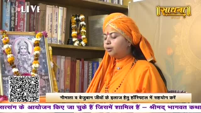 A woman in saffron robes speaks, her head adorned with a matching turban. Behind her, bookshelves overflow with volumes, and a framed image of a deity, draped with marigold garlands, sits on a table. A woman in saffron robes speaks, her head adorned with a matching turban. Behind her, bookshelves overflow with volumes, and a framed image of a deity, draped with marigold garlands, sits on a table.
