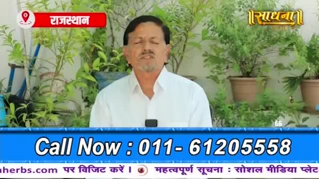 A man in a white shirt speaks, framed by lush green plants. A red banner identifies the location as Rajasthan, and a golden logo for Sadhna appears above the foliage. A man in a white shirt speaks, framed by lush green plants. A red banner identifies the location as Rajasthan, and a golden logo for Sadhna appears above the foliage.