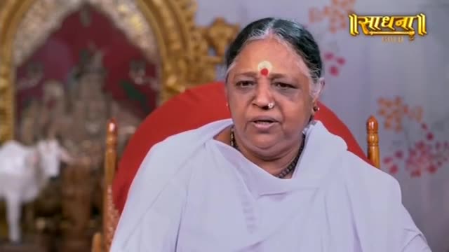 A woman in white, her forehead marked with a red bindi, speaks directly to the camera. Behind her, a shrine with a white cow and ornate carvings hints at a spiritual setting in India. A woman in white, her forehead marked with a red bindi, speaks directly to the camera. Behind her, a shrine with a white cow and ornate carvings hints at a spiritual setting in India.