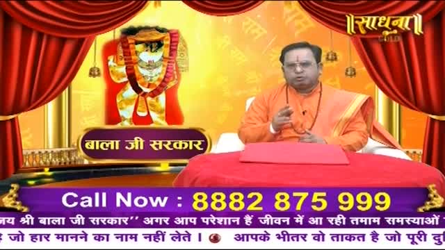 A man in an orange robe speaks with his hands animated. Behind him, a vibrant depiction of a deity is displayed. A phone number flashes across the bottom of the screen.