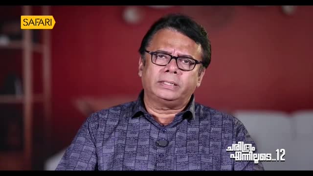 The man in glasses is speaking, his expression serious. A "Safari" logo is visible, and text in Malayalam is on the screen, suggesting a program from India.
