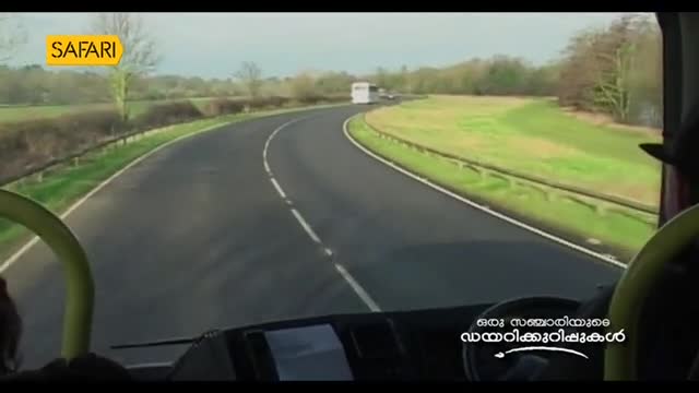 A bus curves along a country road, the view framed by the driver's seat and a Safari TV logo. Ahead, another vehicle navigates the bend, disappearing into the distance.
