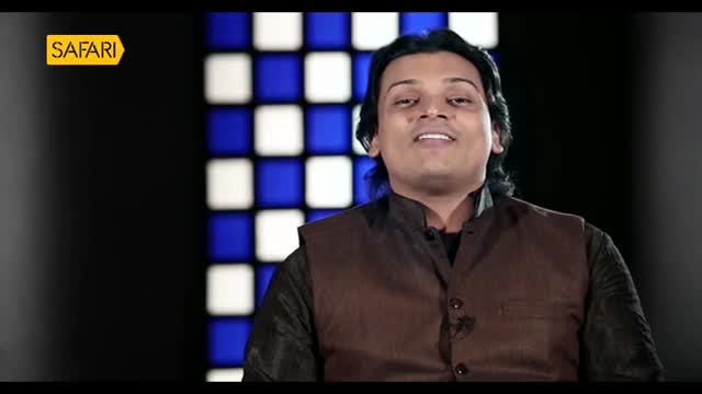 A man in a brown vest is speaking, likely for Safari TV in India, with a backdrop of blue and white squares. His expression is animated, and he seems to be mid-sentence.
