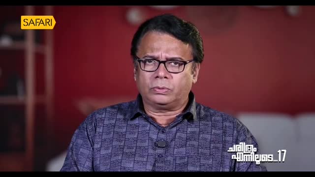 A man in glasses, likely on Safari TV, stares directly into the camera. The red background and the logo suggest a studio setting in India.
