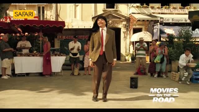 A man in a suit and wig is dancing in the middle of the square, while onlookers watch from the sides. The Safari TV logo sits in the corner, and the scene appears to be from a movie.
