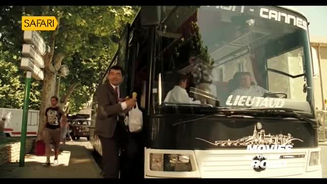 A man in a suit is stepping down from a bus, holding a baguette and a shopping bag. The bus, marked with "Cannes" on top, is parked near a sign for Safari.

