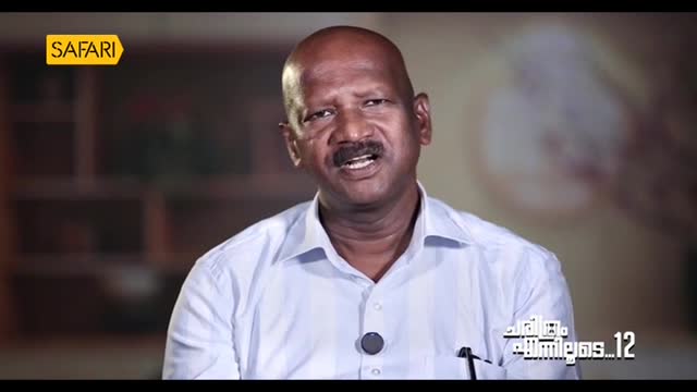 A man with a bald head and a dark mustache is speaking, his mouth open in mid-sentence. The Safari TV logo is visible in the corner, and text in a script I don't understand is below.
