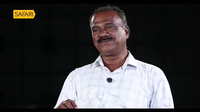 A man in a checkered shirt smiles slightly, gesturing with his hand. The Safari TV logo is visible in the corner, suggesting a broadcast from India.
