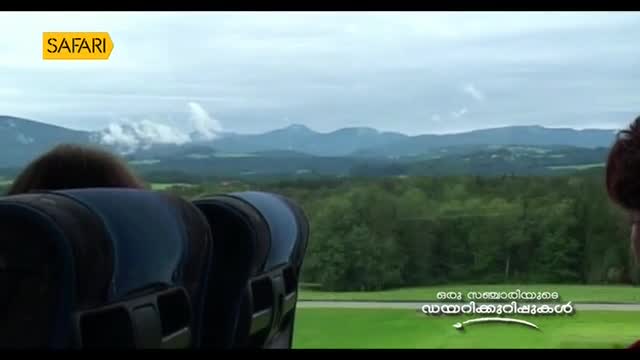 The view from the bus window reveals a vast, green landscape under a cloudy sky. Through the Safari TV broadcast, the scene of mountains and forests unfolds.
