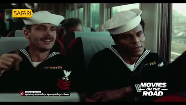 Two sailors in crisp white hats and navy uniforms are seated on a train, with one gesturing as he speaks. The Safari TV logo is in the corner, and the "Movies on the Road" title is visible.
