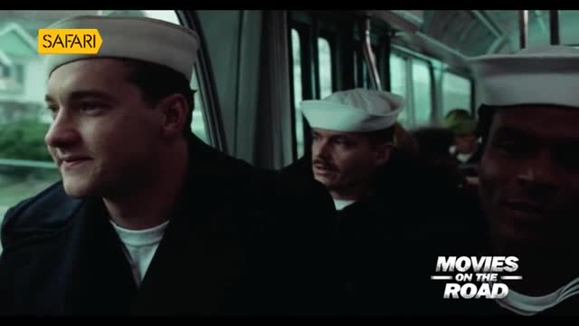 Sailors in white hats and dark jackets ride inside a bus, looking out the windows. The Safari TV logo sits on one of the sailor's hats.
