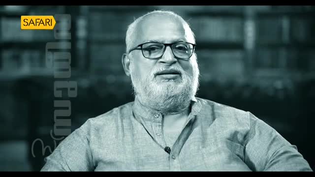 A man with a full white beard and glasses is speaking, likely for a show on Safari TV in India. The background is blurred, but the focus is clearly on the man's face as he talks.
