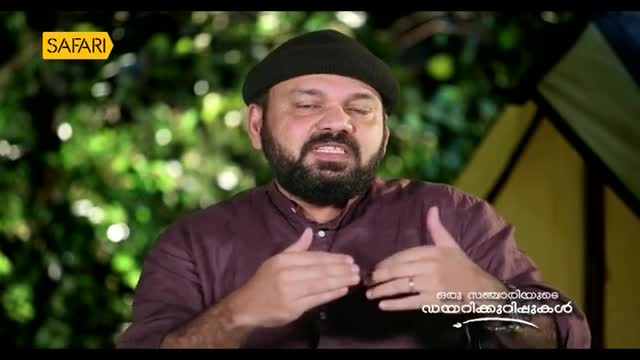 A man in a black cap and maroon shirt gestures with his hands as he speaks. The Safari TV logo is visible in the upper left corner.
