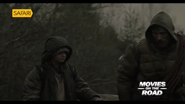 Two figures, both in hooded jackets, stand in a misty, wooded area. The Safari TV logo is in the corner, and the words "Movies on the Road" are visible at the bottom.

