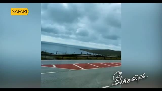 The road stretches ahead, marked with red and white stripes. A gray sky hangs over the ocean, as seen on Safari TV.
The road stretches ahead, marked with red and white stripes. A gray sky hangs over the ocean, as seen on Safari TV.