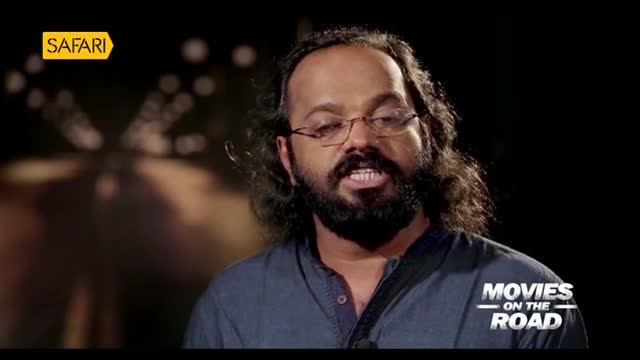 A man with a beard and glasses is speaking, his mouth open as if mid-sentence. The "Safari" logo sits in the top left, and "Movies on the Road" is visible on the bottom right.
A man with a beard and glasses is speaking, his mouth open as if mid-sentence. The "Safari" logo sits in the top left, and "Movies on the Road" is visible on the bottom right.