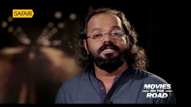 A man with a beard and glasses is speaking, his gaze directed towards the camera. The Safari TV logo is visible in the corner, and the words "Movies on the Road" are displayed below him.
A man with a beard and glasses is speaking, his gaze directed towards the camera. The Safari TV logo is visible in the corner, and the words "Movies on the Road" are displayed below him.