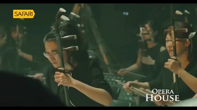 A group of musicians, seen on Safari TV, are focused on playing stringed instruments. They're bowing their instruments, the sound echoing in the Opera House.
