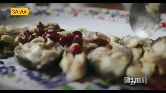 On a floral-patterned plate, a dish of sliced fish is topped with red berries and nuts. A large spoon hovers above the food, perhaps about to serve it.
