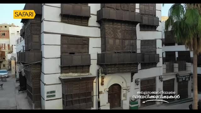 A white building with dark wooden balconies and window frames stands tall, framed by a palm tree on the right. The Safari TV logo is visible in the top left corner, and text in Malayalam is displayed on the lower right.
A white building with dark wooden balconies and window frames stands tall, framed by a palm tree on the right. The Safari TV logo is visible in the top left corner, and text in Malayalam is displayed on the lower right.
