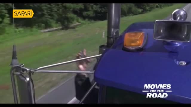 A blue truck, part of the "Movies on the Road" series, speeds along a green, tree-lined road. A hand reaches out, possibly trying to grab something, as the vehicle moves forward.
A blue truck, part of the "Movies on the Road" series, speeds along a green, tree-lined road. A hand reaches out, possibly trying to grab something, as the vehicle moves forward.