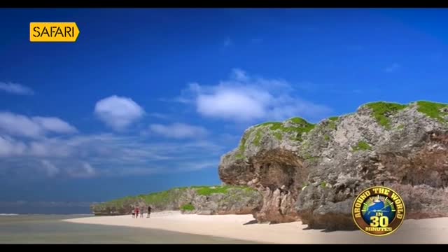 A bright blue sky stretches above a sandy beach, where a few people stroll near some rocky cliffs covered in green vegetation. The Safari TV logo is in the top left corner, and the bottom right corner shows the "Around the World in 30 Minutes" logo.
A bright blue sky stretches above a sandy beach, where a few people stroll near some rocky cliffs covered in green vegetation. The Safari TV logo is in the top left corner, and the bottom right corner shows the "Around the World in 30 Minutes" logo.