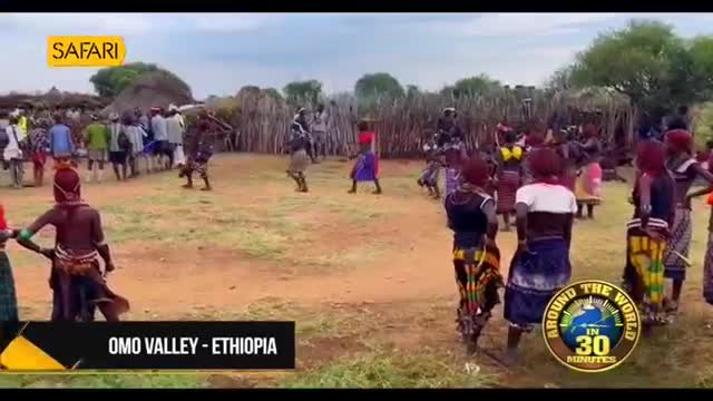 A group of people in colorful attire are gathered in a dusty clearing, some dancing. The "Safari" logo and "Omo Valley - Ethiopia" text overlay suggest this is a scene from a documentary.