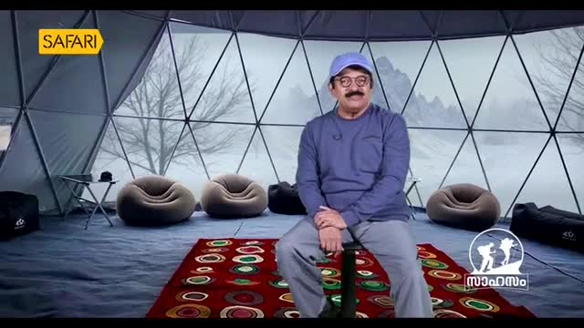 A man in a blue shirt and cap sits on a stool in a geodesic dome, a red rug beneath him. The Safari TV logo is visible in the upper left corner.