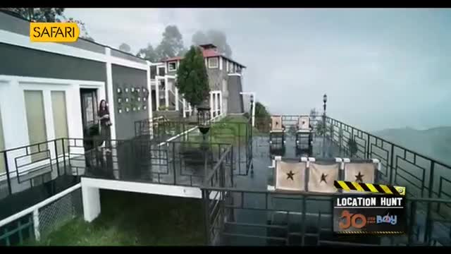A woman stands on a wet balcony overlooking a misty valley. The "Safari" logo is visible on the building, and a "Location Hunt" sign sits on the railing.