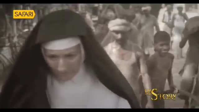 A woman in a nun's habit walks through a crowd in what looks like a scene from India. A young boy with a wide grin runs alongside her.