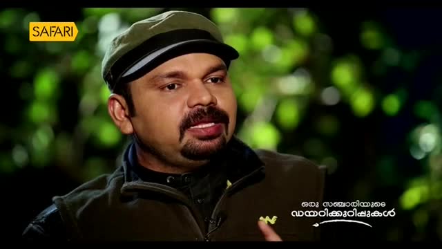 A man with a goatee and a cap speaks, his face illuminated against a blurred green background. The Safari TV logo appears in the upper left corner.