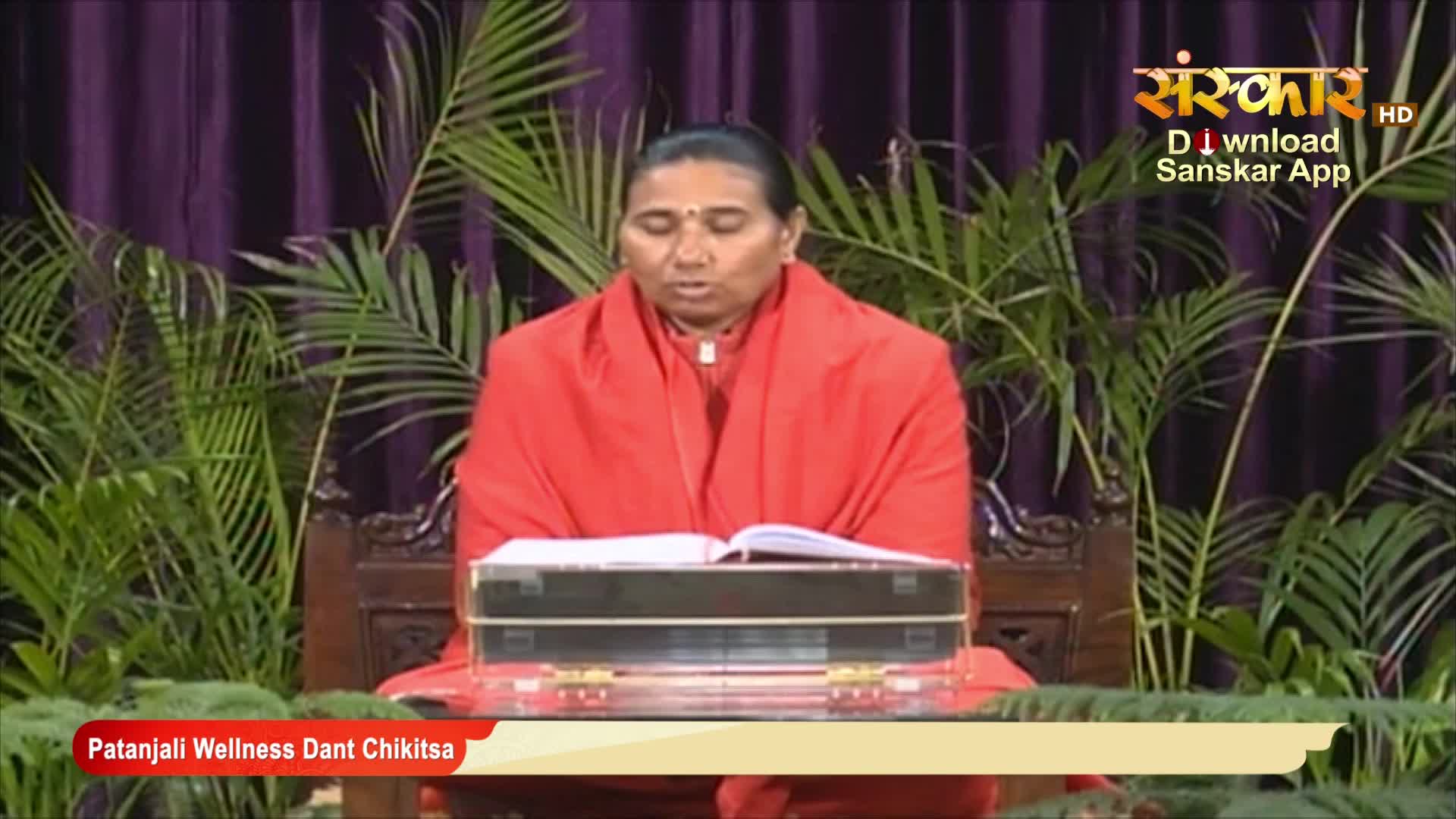 A woman in a red robe sits behind a table, reading from an open book. The Sanskar TV logo is visible in the upper right corner, and the lower banner reads "Patanjali Wellness Dant Chikitsa."
