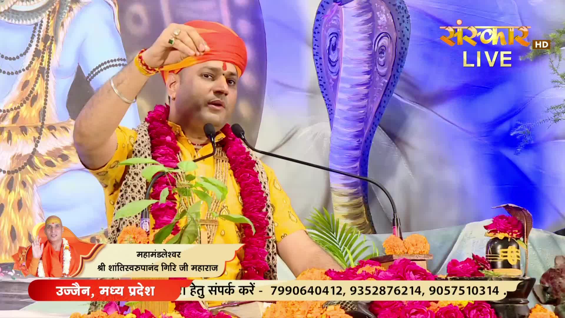 A man in a saffron turban gestures while speaking into a microphone. The broadcast is live on Sanskar TV, with text at the bottom identifying him as a spiritual leader from Ujjain, India.
