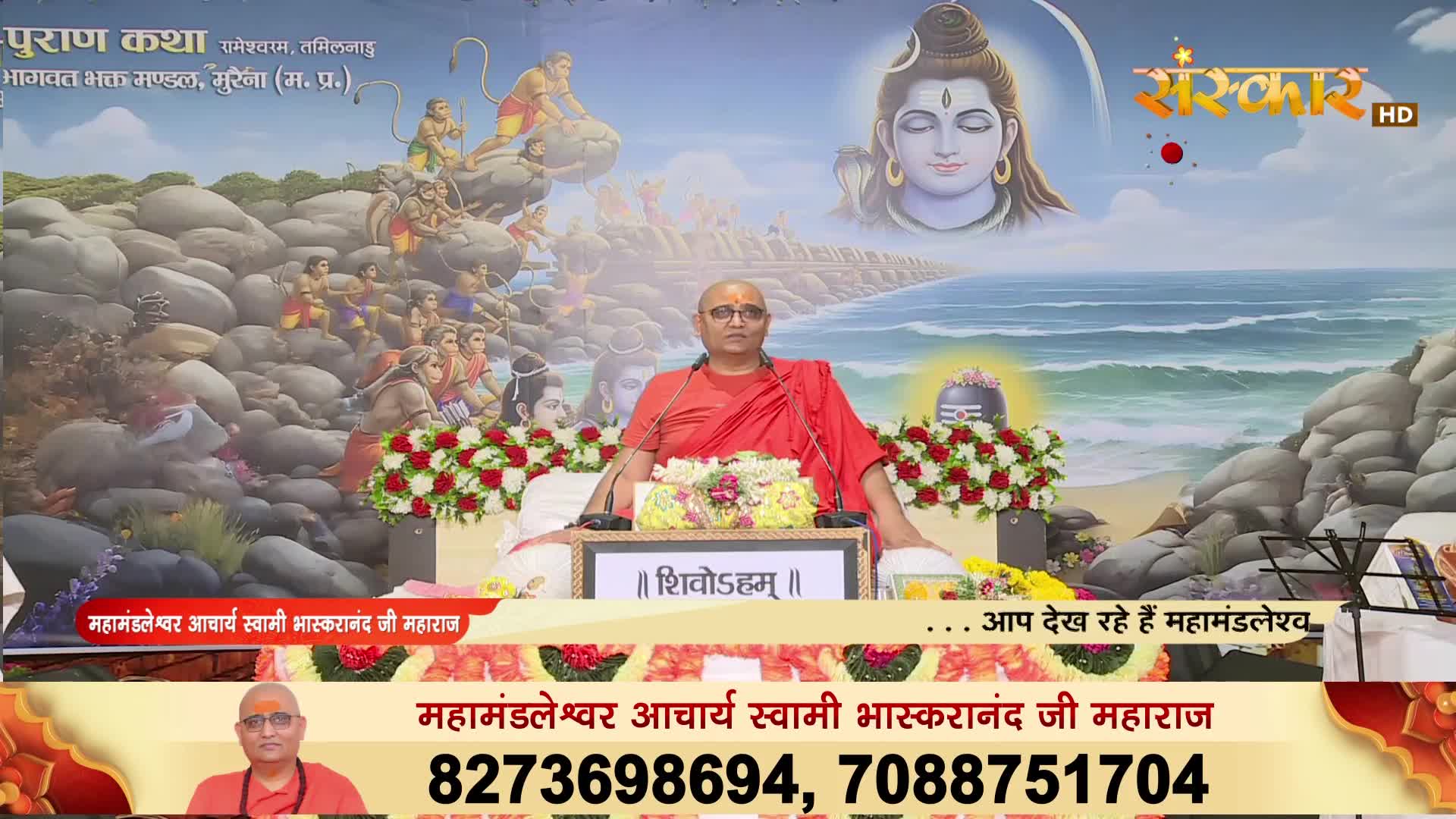 A man in a red robe sits behind a small podium, speaking into a microphone. The scene is broadcast on Sanskar TV, with a backdrop of a painting depicting religious figures and a serene image of a deity.
