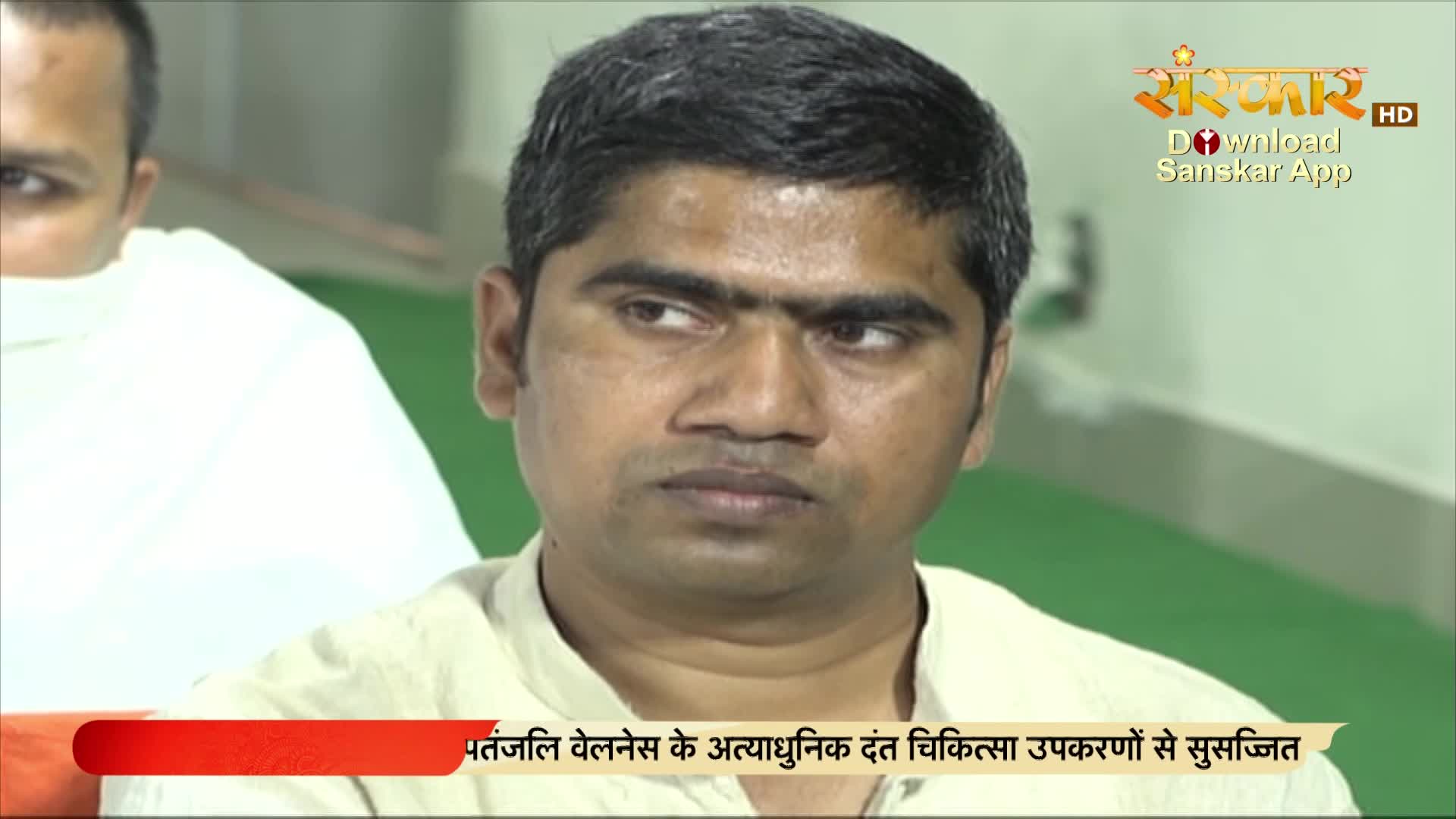 A man with dark hair and a serious expression is looking off-camera, likely during a broadcast on Sanskar TV. Below him, a red banner with Hindi text is visible.
