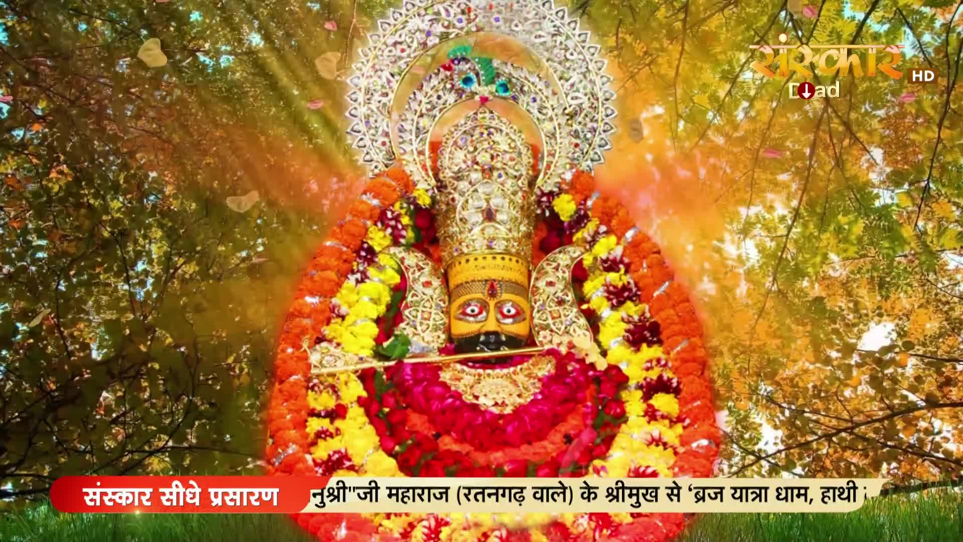 A richly adorned deity, framed by garlands of flowers, is the focus of the scene. Sunlight filters through the trees, and the Sanskar TV logo is visible in the upper right.
