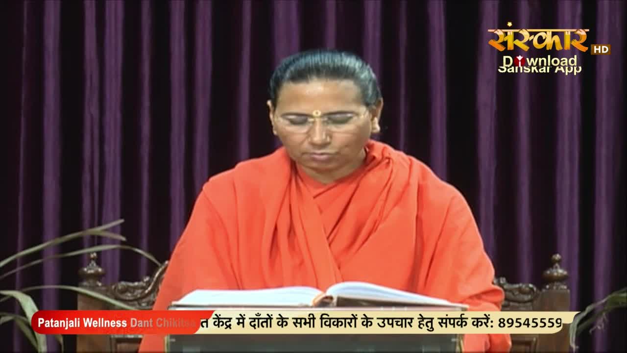 A woman in an orange robe sits at a table, reading from an open book. The Sanskar TV logo is visible in the corner, and text about a dental clinic runs along the bottom of the screen.
