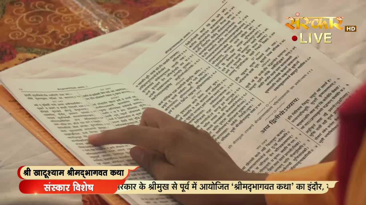 A hand, with a pale complexion, traces a line of text on a large, open book. The Sanskar TV logo is visible, broadcasting from India, as the book is being read.
