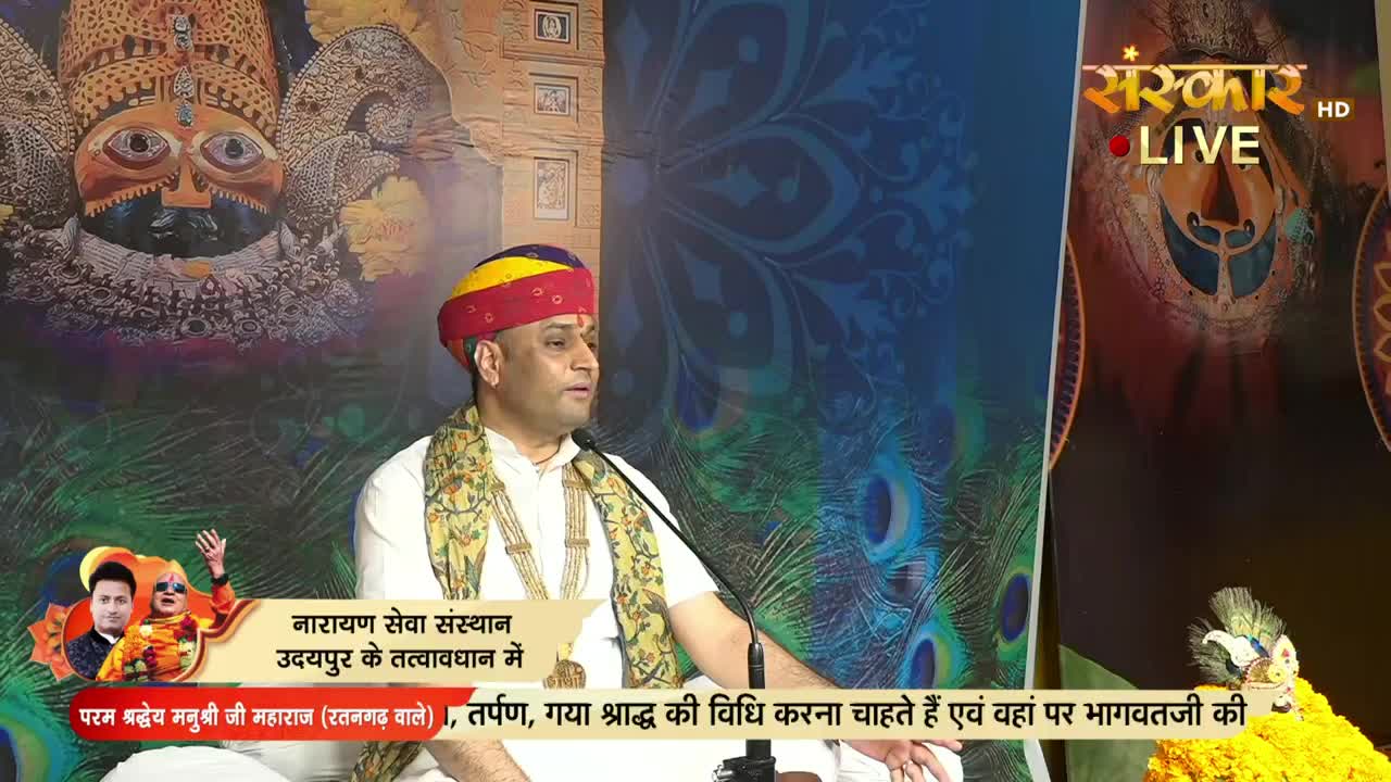 A man in a turban and scarf speaks into a microphone, framed by a peacock feather backdrop. The Sanskar TV logo is visible, and a banner below mentions a service in Udaipur.
