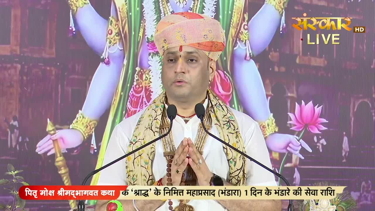 A man in a turban and shawl stands at a podium, his hands clasped in prayer. Behind him, a backdrop featuring a deity is visible, and the Sanskar TV logo is in the corner.
