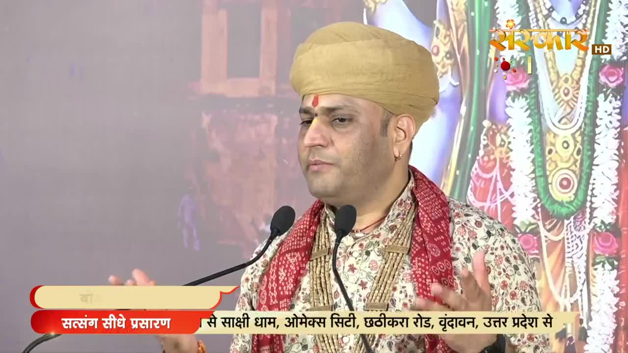 A man in a turban and ornate clothing gestures with his hands, speaking into two microphones. The broadcast logo for Sanskar TV is visible in the corner, with Hindi text below.
