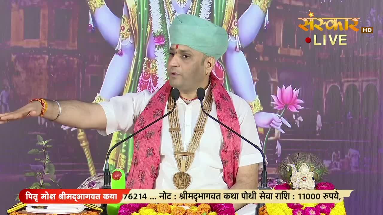 A man in a turban and ornate jewelry gestures with his right arm, speaking into two microphones. The Sanskar TV logo is visible, and the backdrop features a deity and a lotus flower.
